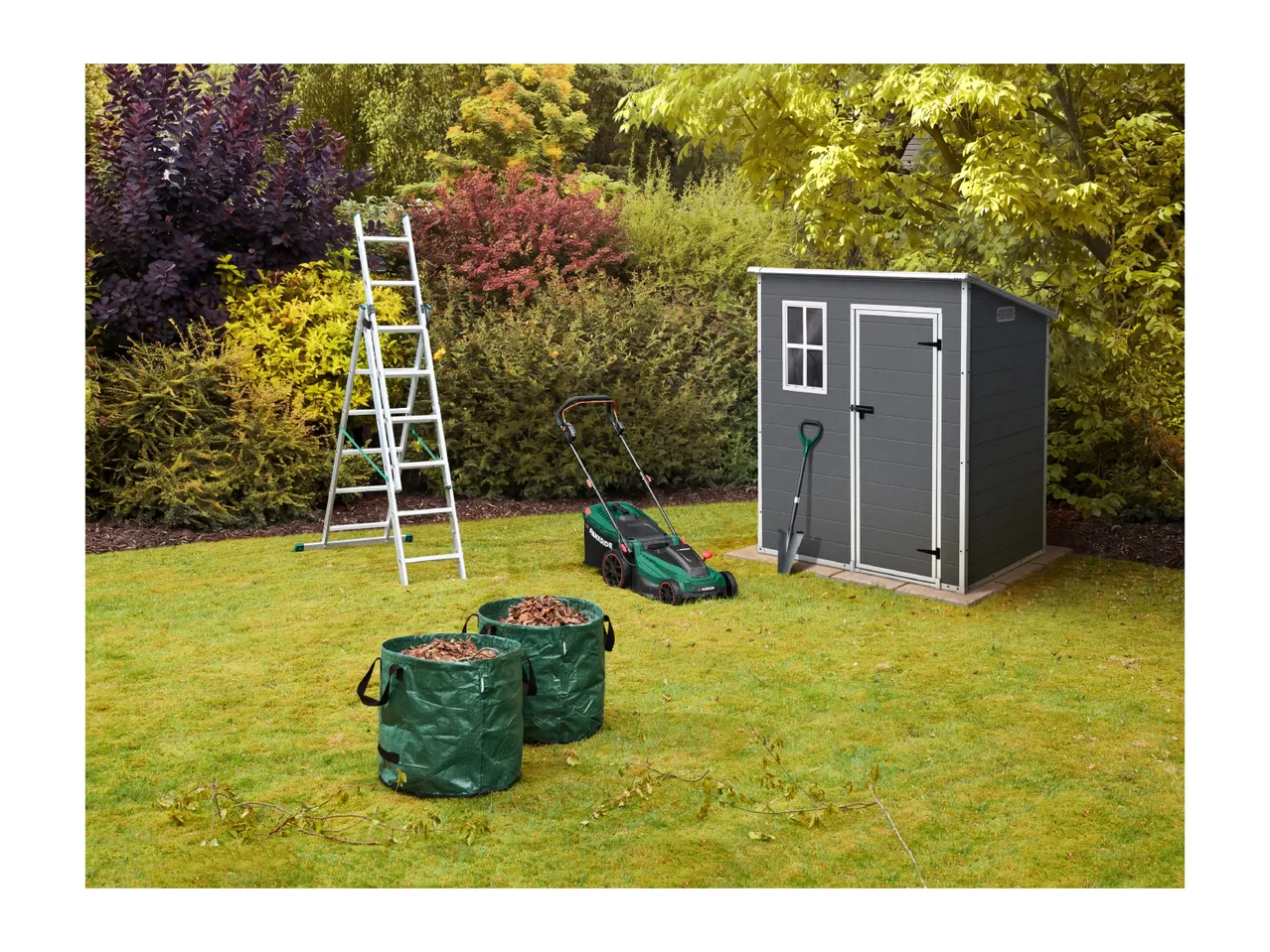 Garden shed, lawnmower, and ladder in a garden setting with foliage bags.