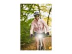 Woman in a pink cycling jacket, helmet, and sunglasses riding an electric bike on a path.