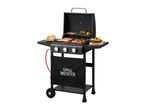 Black gas grill with food cooking on the grates, including sausages, meat, and vegetables.