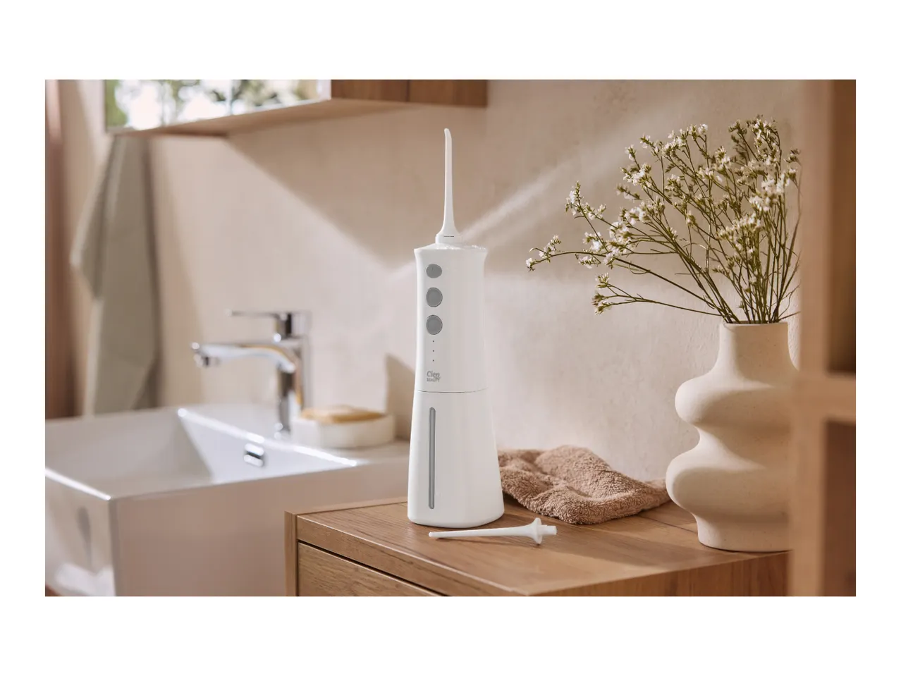White oral irrigator on a wooden bathroom counter with a sink and flowers in the background.
