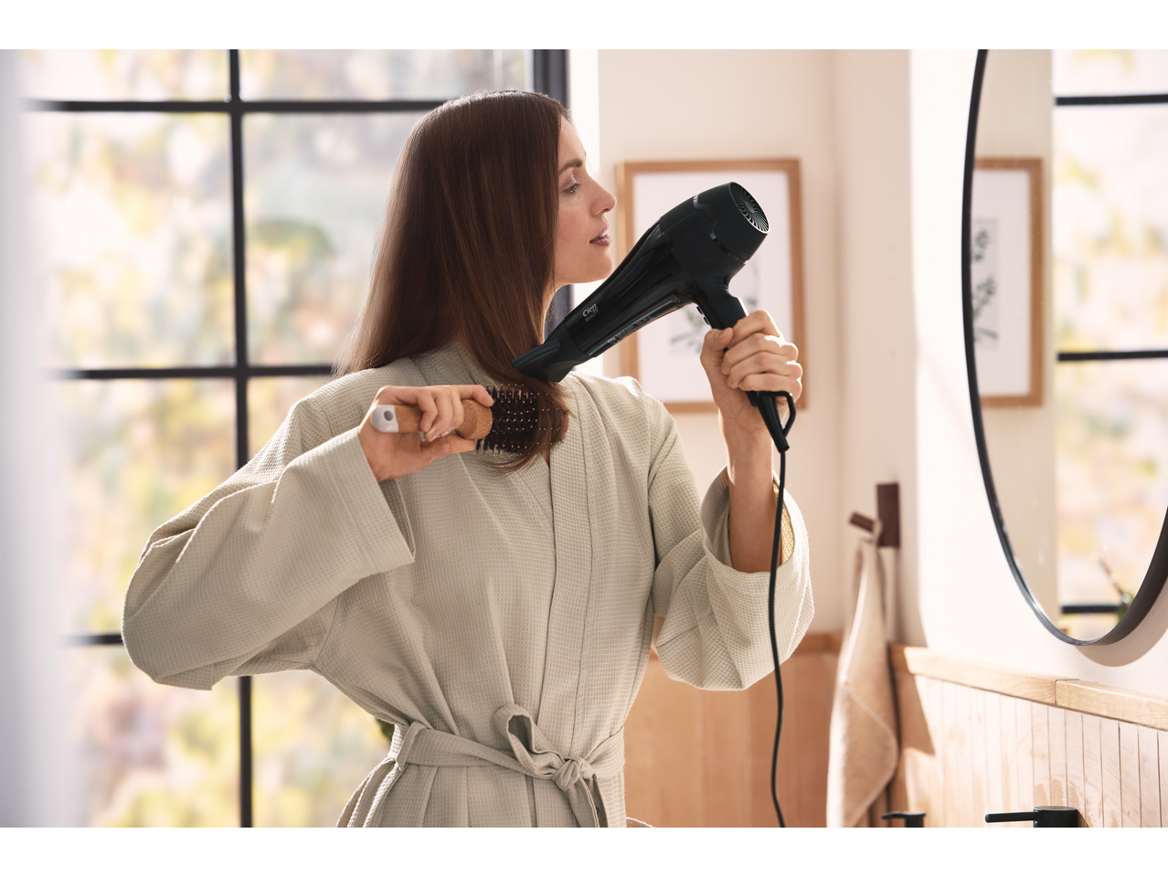 Femeie își usucă părul cu un uscător de păr CIEN BEAUTY și o perie.