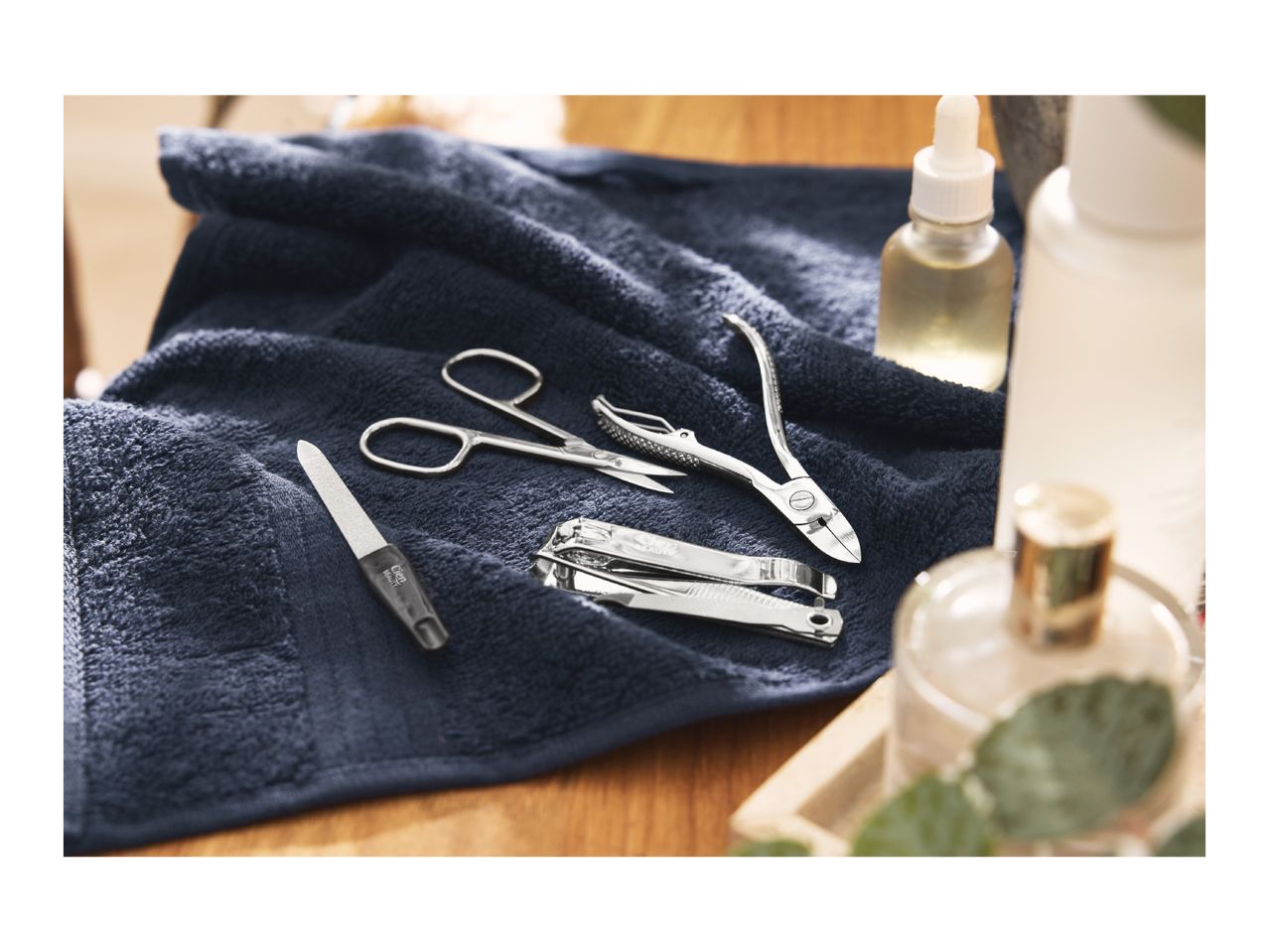 Manicure set with nail clippers, cuticle nippers, scissors, and a nail file on a dark blue towel.