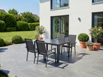 Conjunto de jantar exterior com quatro cadeiras e uma mesa num pátio junto a uma casa com jardim.