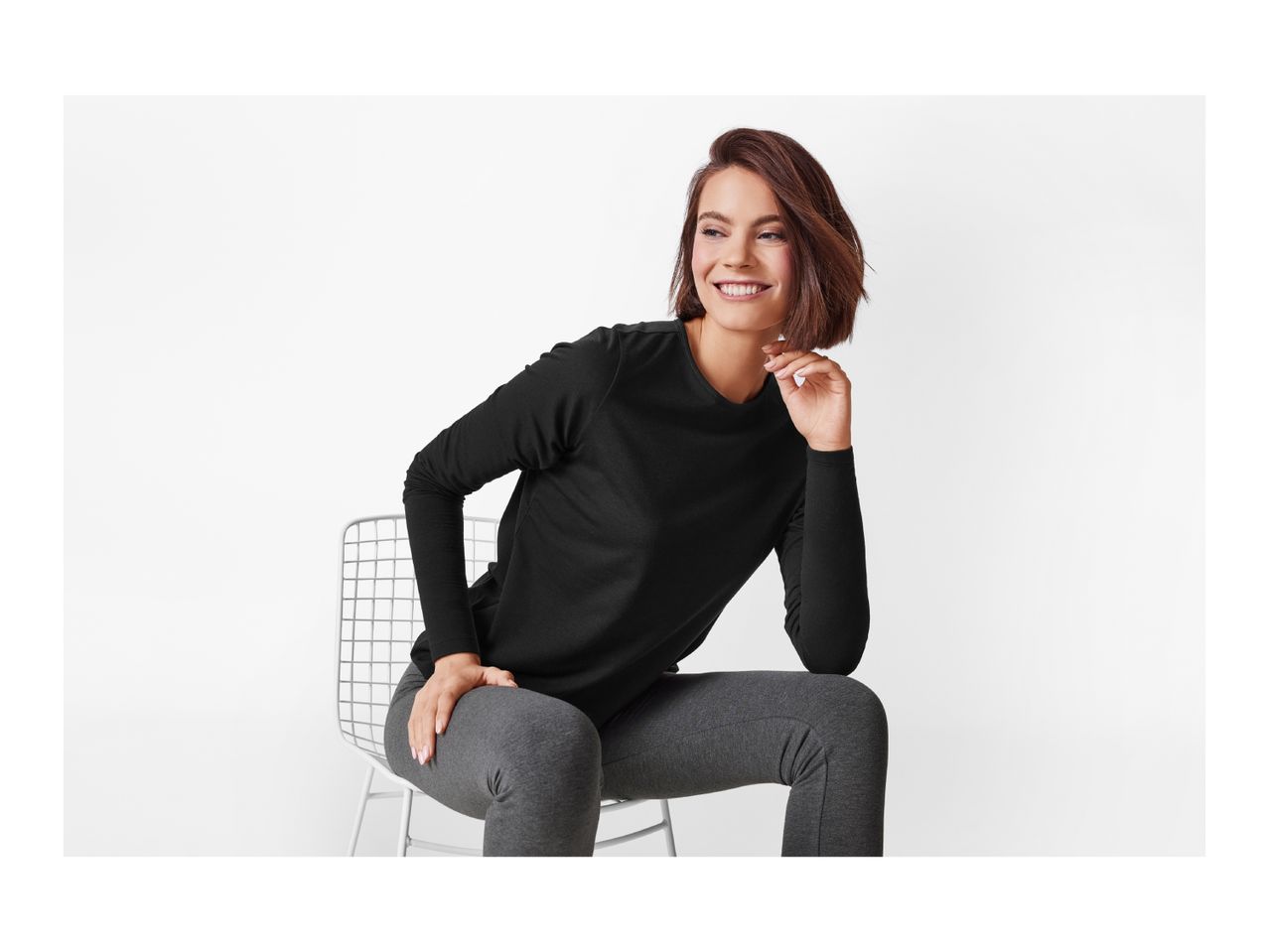 A woman in a black long-sleeve shirt and gray leggings sits on a chair.