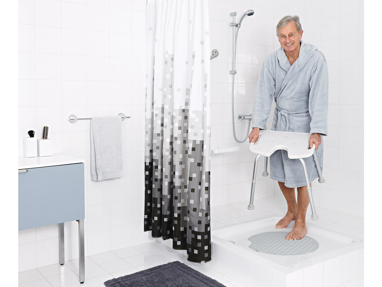 Smiling man in a bathrobe with a RIDDER® shower chair in a modern bathroom.