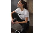 Woman in white t-shirt and black leggings holding a water bottle, resting after a workout.