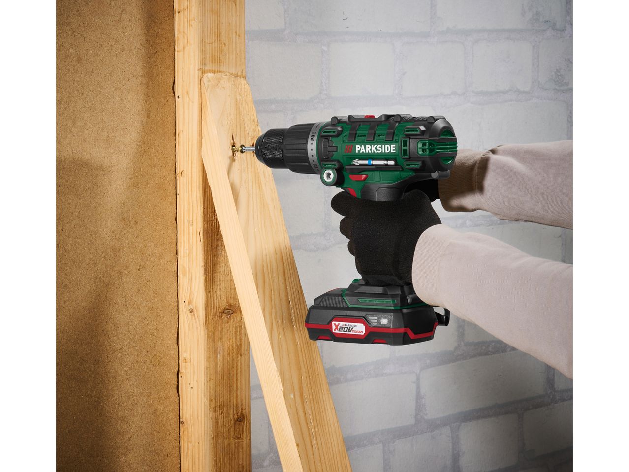 Un uomo utilizza un trapano a percussione Parkside X20V Team per fissare un pezzo di legno.