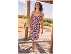 Une femme en robe d'été à motif animalier et sac de plage en paille sur une terrasse en bois.