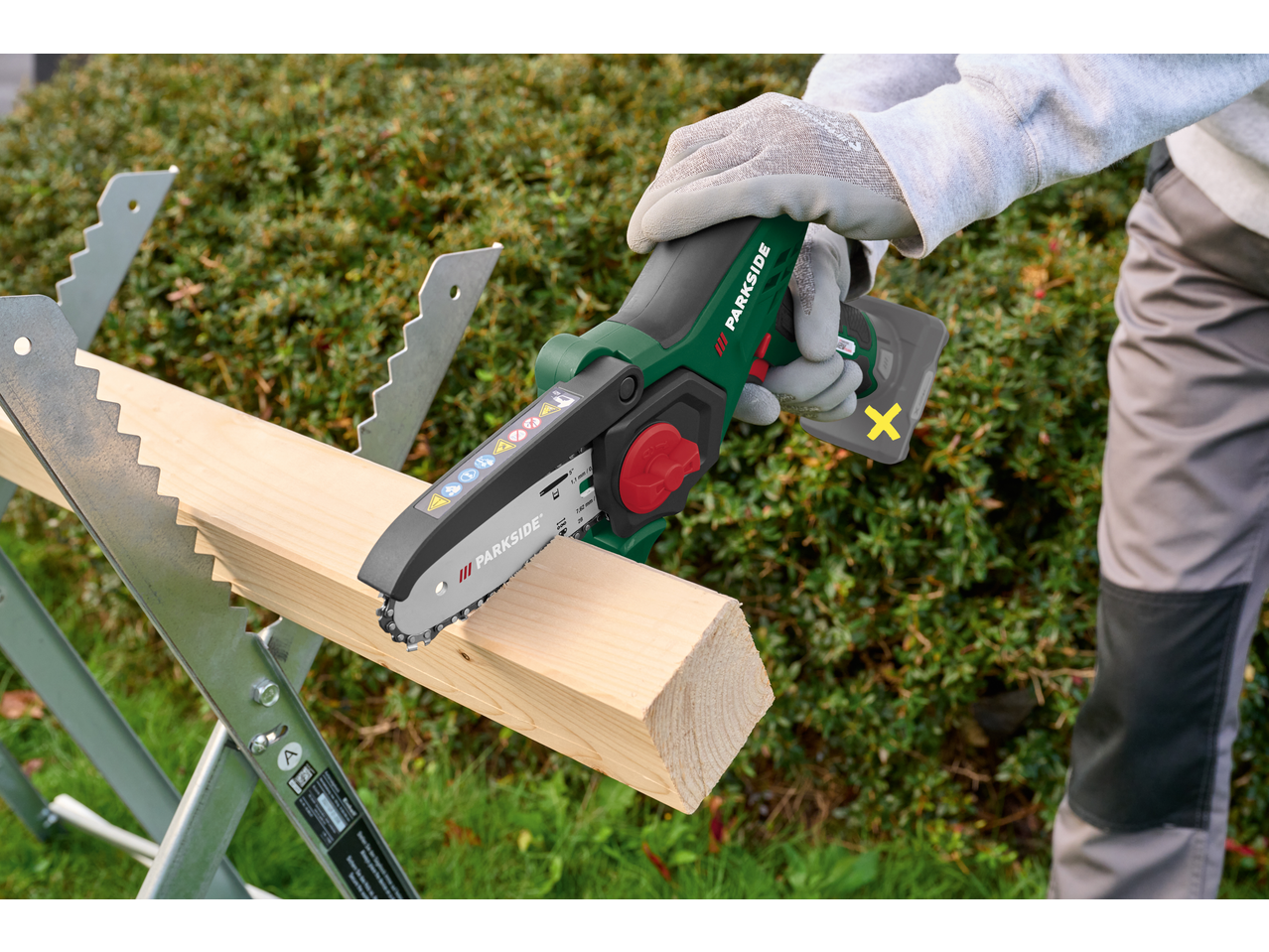 Mini fierăstrău cu lanț PARKSIDE tăind lemn pe un capră, cu mănuși de lucru.