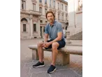 Homem de polo azul e calções azul-marinho sentado num banco de pedra.