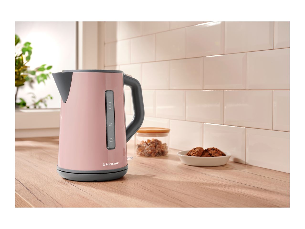 A pink SilverCrest electric kettle on a wooden kitchen counter with cookies and sugar.