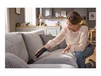 Woman cleaning a grey sofa with a black handheld vacuum cleaner in a modern living room.