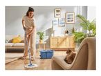 Woman mopping a wooden floor with a blue mop and bucket in a living room with a cat.