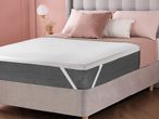 A bed with a white mattress topper, gray mattress, and pink bedding in a bedroom.