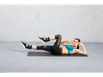 Woman doing crunches with CRIVIT ankle weights on a yoga mat.
