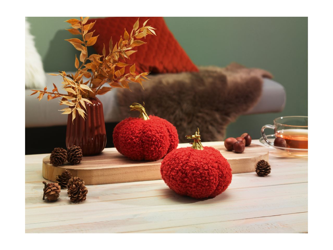 Autumnal decor with red pumpkins, dried leaves, pinecones, and a cup of tea.