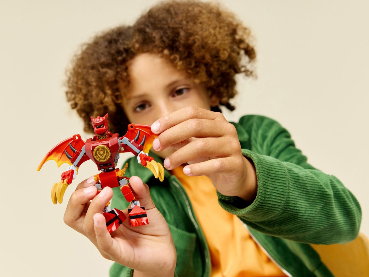 A child holding a red and yellow toy dragon, wearing a green jacket.