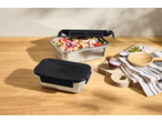 Two stainless steel lunchboxes, one open with a bean salad, on a wooden table with red onions.