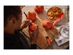A person carving a small pumpkin on a wooden board with carving tools nearby.
