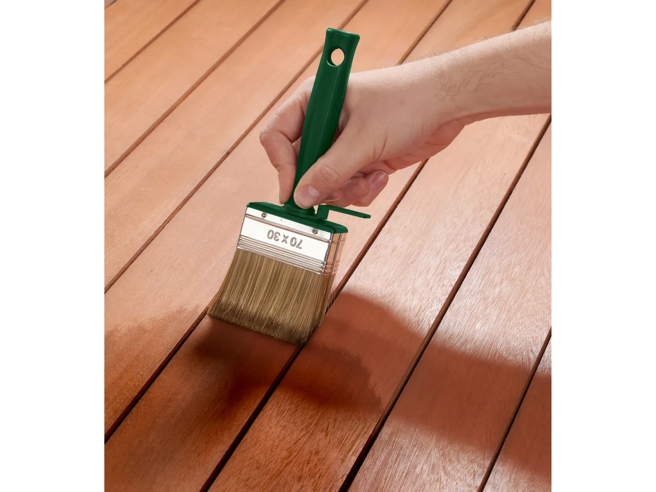 Una mano applica vernice a un pavimento di legno con un pennello.