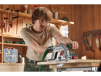 A man in a workshop using a Parkside circular saw to cut wood, with sawdust in the air.
