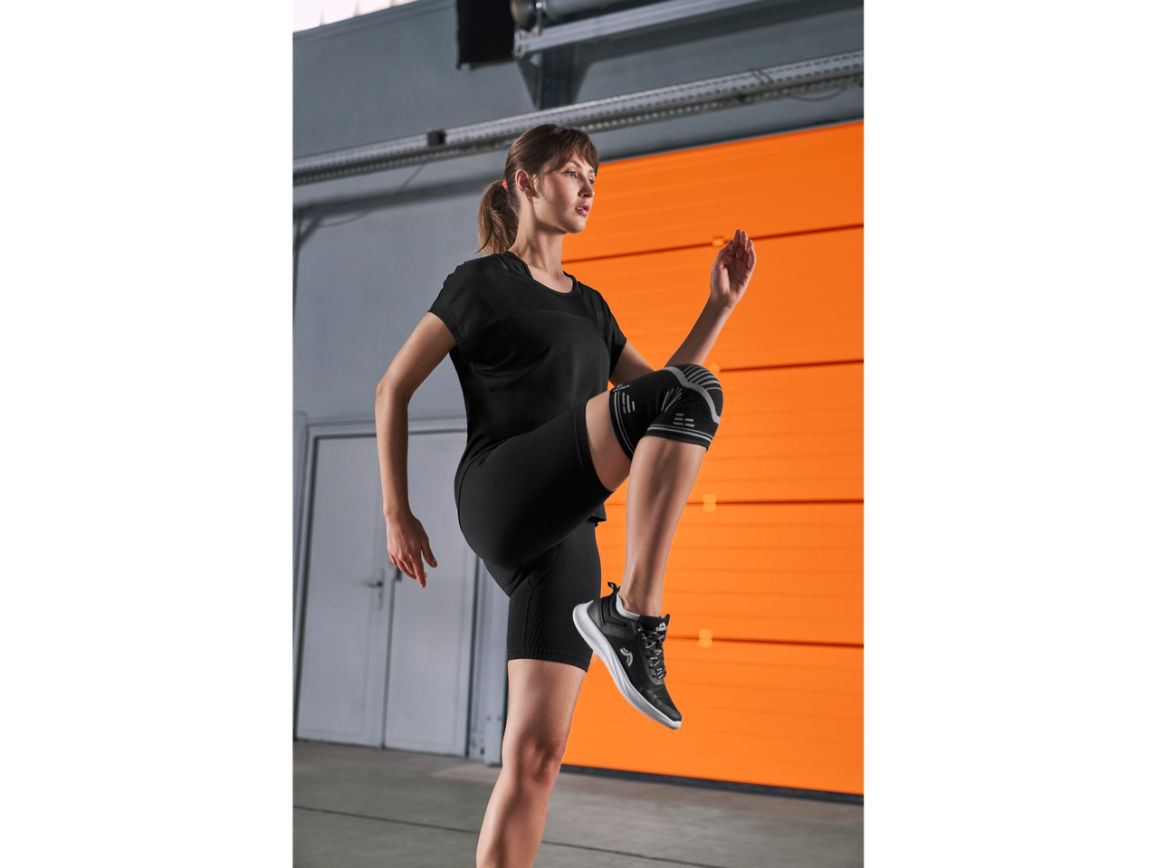 Γυναίκα με μαύρα αθλητικά ρούχα και επιγονατίδα Crivit, κάνει άσκηση.