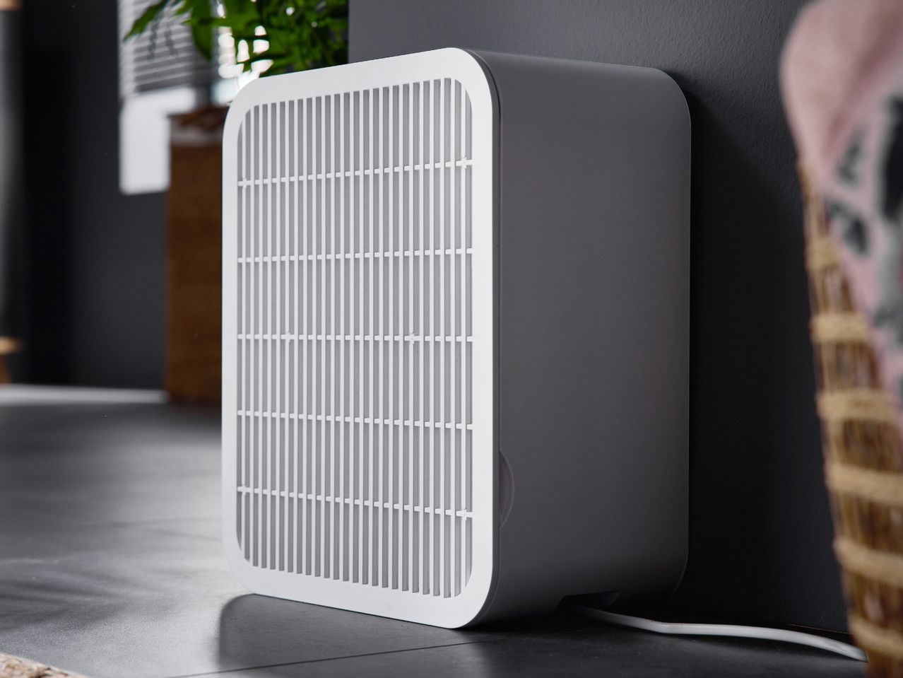 White and gray air purifier on a dark floor next to a wall