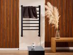 Fekete törölközőszárító radiátor barna törölközővel, fa panelekkel és pampafűvel.