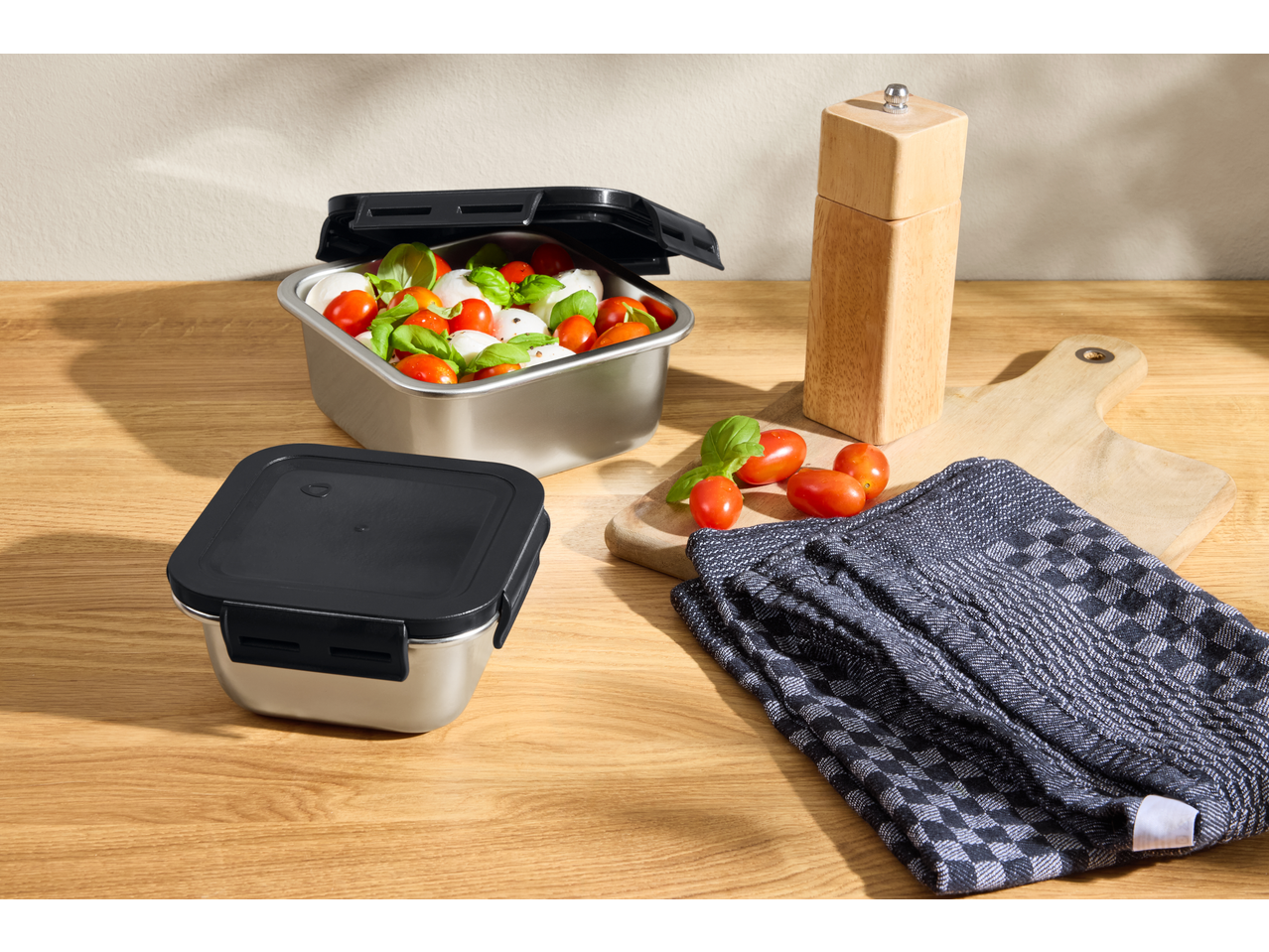 Recipiente din oțel inoxidabil cu capac, cu salată caprese, pe o masă de lemn.