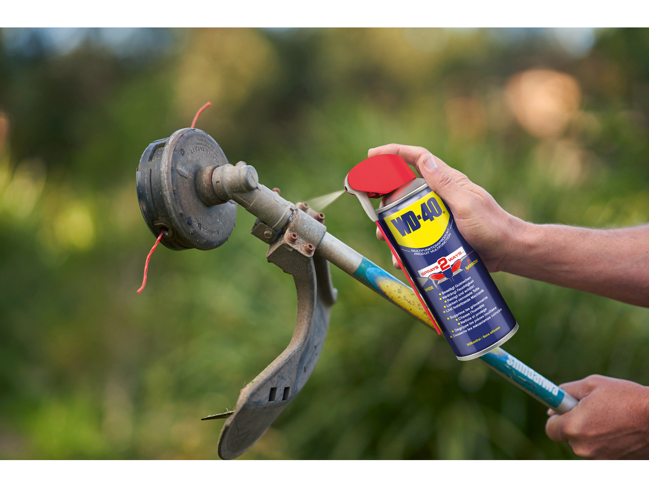 Pessoa a pulverizar WD-40 num aparador de relva para o lubrificar.