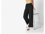 Pantaloni largi negri cu talie elastică, model pozând lângă un scaun metalic.