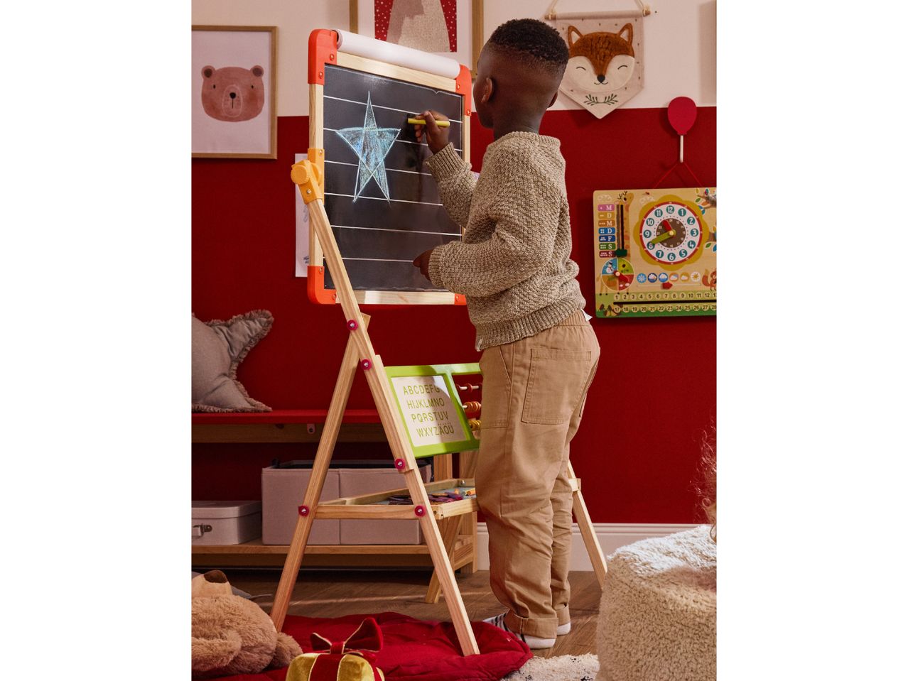 A child drawing on a chalkboard easel in a playroom with a calendar and animal-themed decor.