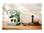 A mint green SilverCrest espresso machine brewing coffee into two glasses on a wooden countertop with cookies and coffee beans.