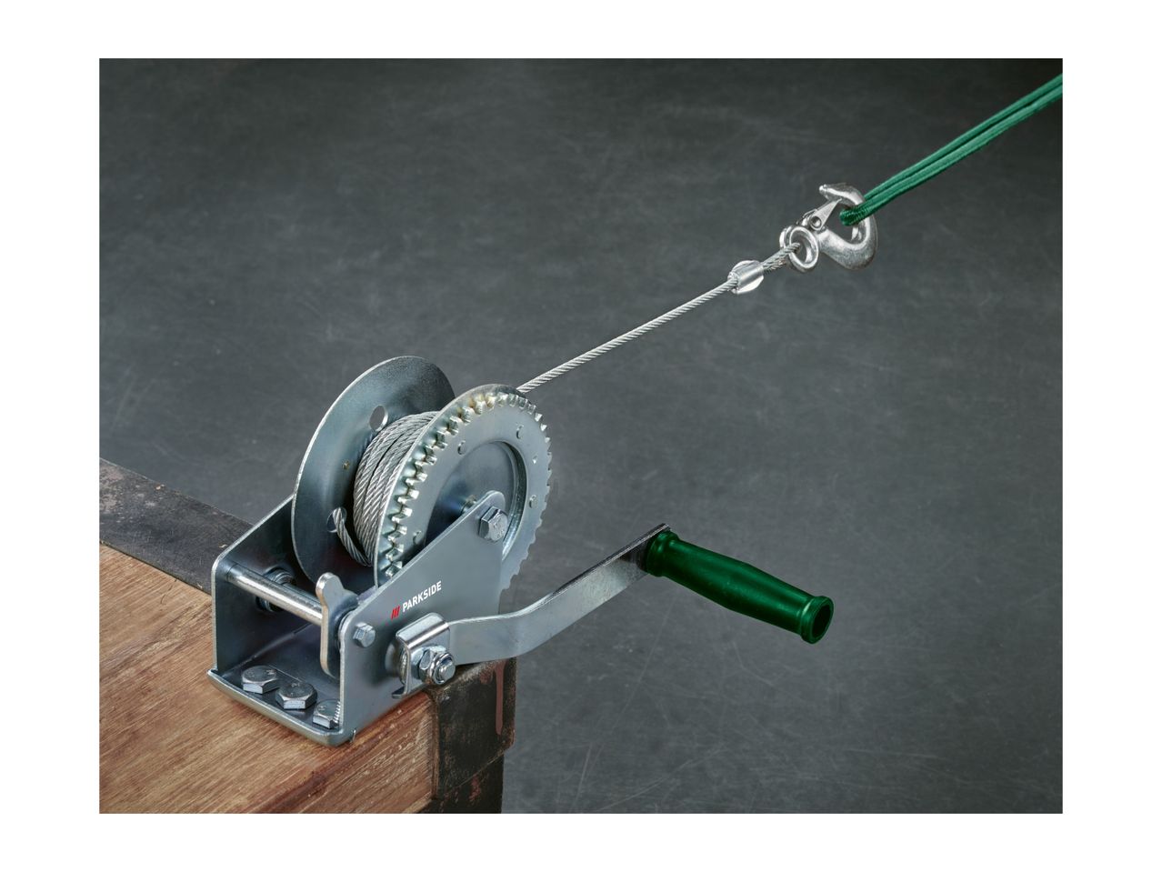 Hand winch with steel cable and hook, mounted on a wooden beam.