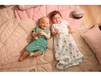 Doi bebeluși fericiți stau pe pături, unul într-un body LUPILU verde și celălalt într-un sac de dormit LUPILU.