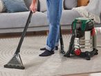 A person uses a Kärcher carpet cleaner to clean a rug.