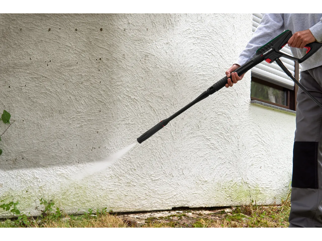 A person uses a Parkside® pressure washer to clean a white wall.