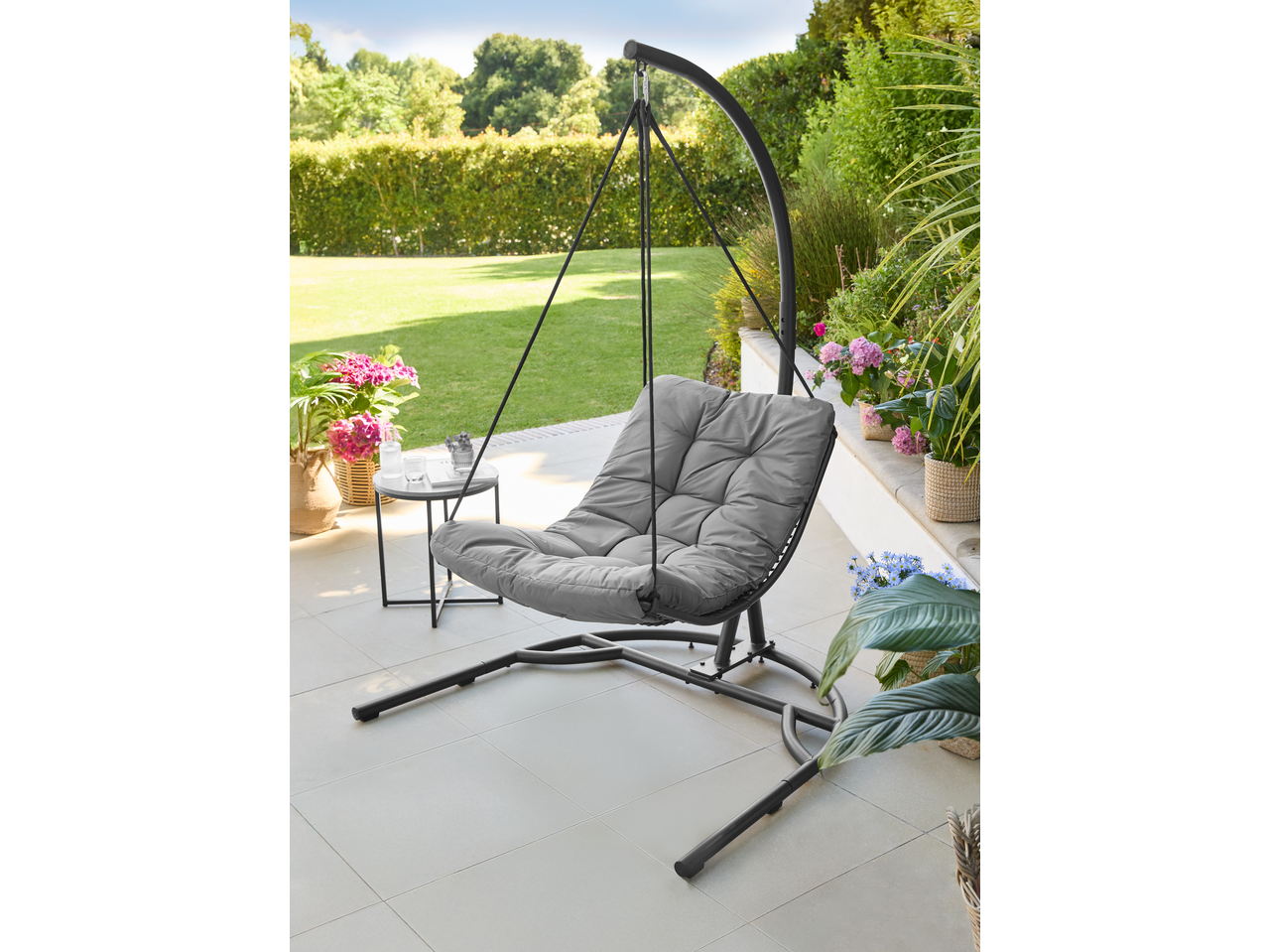 Grey hanging egg chair with a side table and potted plants on a patio.