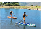 Deux personnes font du paddleboard sur un lac, avec des montagnes et des arbres en arrière-plan.