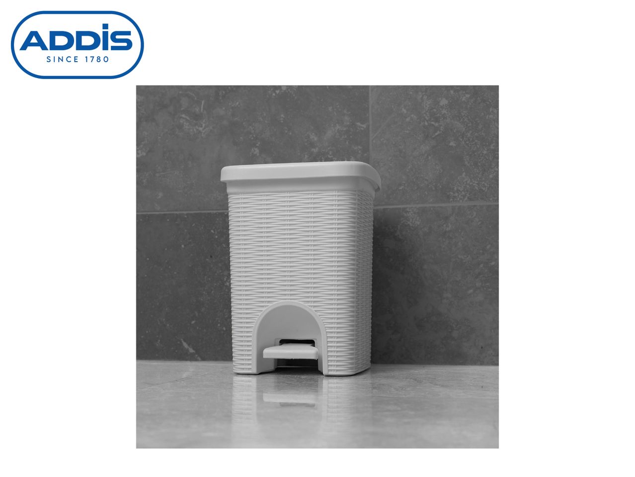 A white Addis step-on trash can sits on a gray surface.