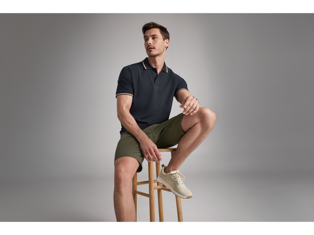 Model masculin cu polo negru și pantaloni scurți verzi.