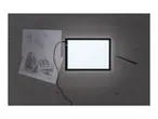 An illuminated light pad for drawing, with hand and landscape sketches, a pencil, and an eraser on a wooden table.