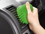 A hand uses green cleaning putty to clean a car's air vent.