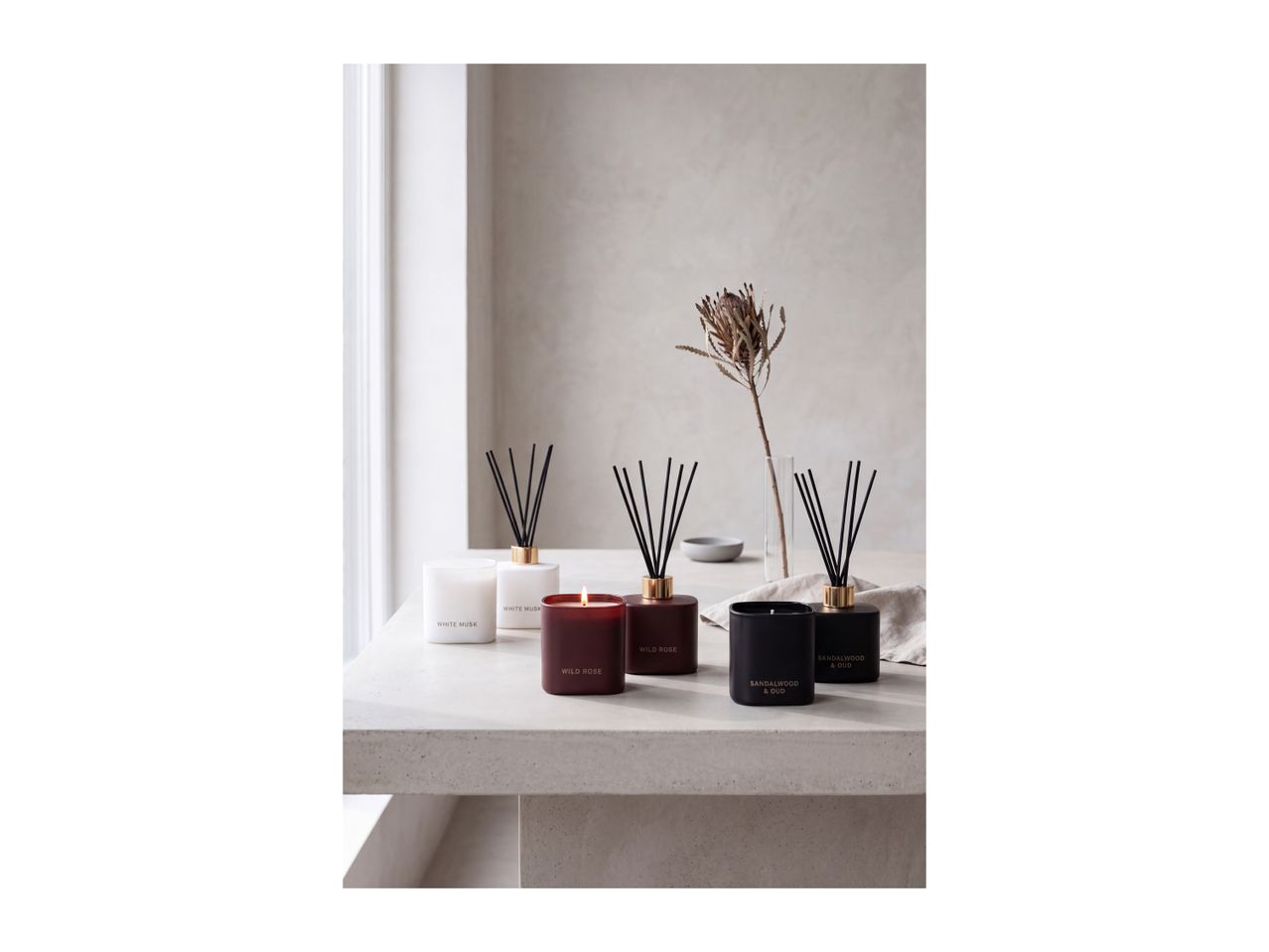Scented candles and reed diffusers in White Musk, Wild Rose, and Sandalwood & Oud on a table.