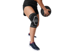 Person wearing a knee support and shorts, holding a medicine ball, with trainers visible.