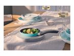 A small turquoise frying pan with green peppers and lemon slices on a table set for dining.