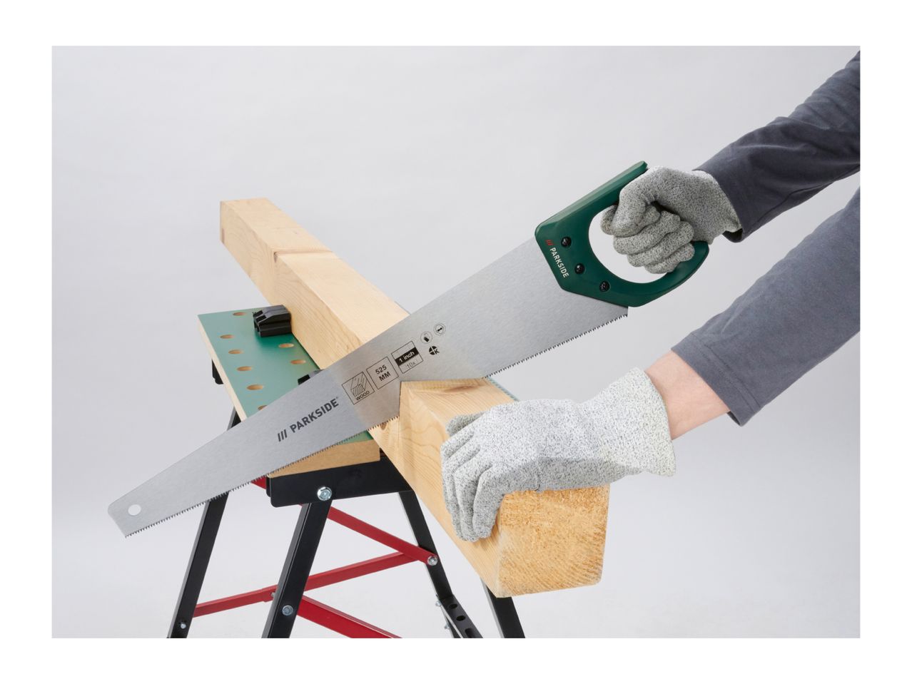 Hands in safety gloves sawing a wooden beam on a workbench with a hand saw.