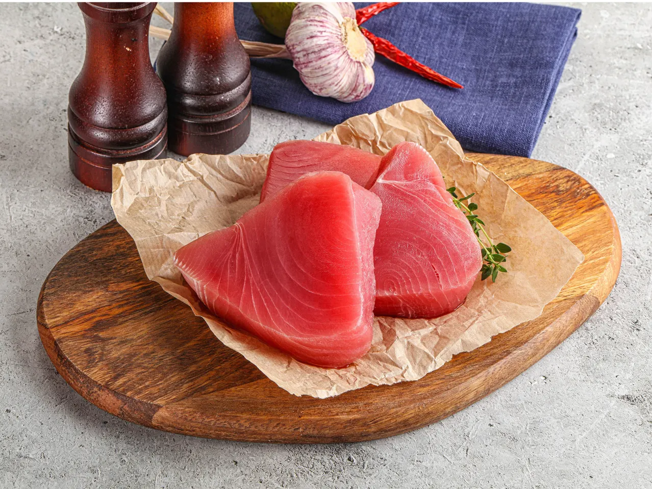 Fresh tuna steaks on parchment paper with spices and a blue napkin.