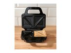 Open sandwich toaster with one toasted sandwich on a wooden surface.