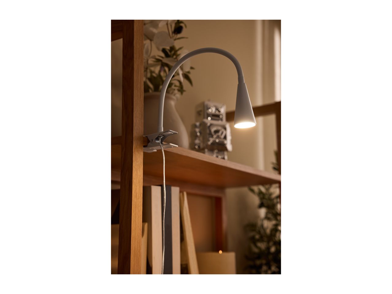Clip-on lamp illuminating a wooden shelf with decorative items and books.